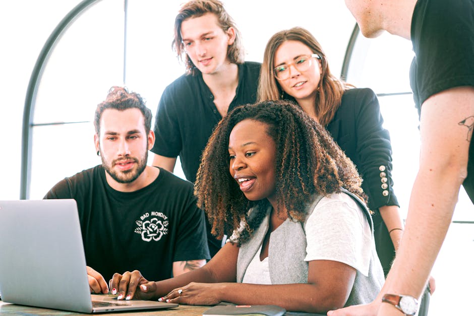 Un groupe diversifié de jeunes professionnels collaborant autour d'un ordinateur portable dans un bureau moderne. Idéal pour des concepts business ou technologiques.