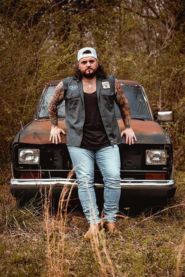 Country-rock artist Jason Cross posing in front of a vintage rustic car.