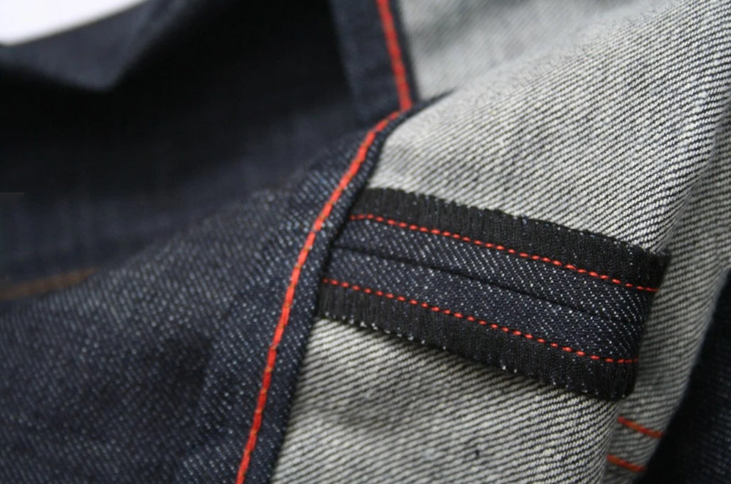 The hem of first the Grand Street raw denim jeans by the Williamsburg Garment Co. brand in 2011. The hem feature the brands trademark orange chain stitching, with orange detail stitching in the coverstitched edge.