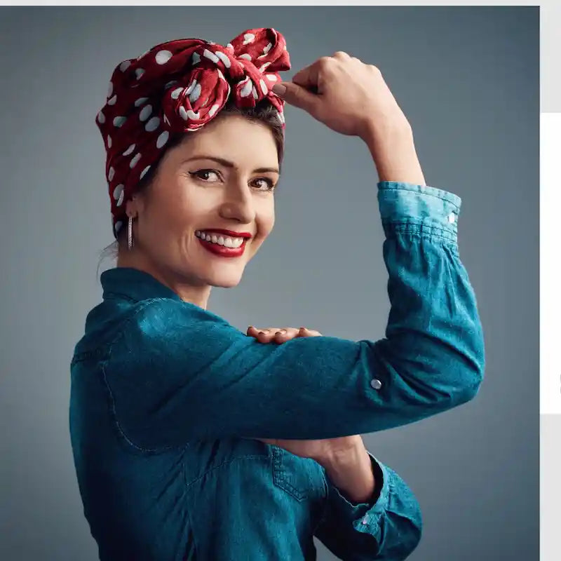 Confident woman in a red polka dot headscarf and denim shirt striking a ‘Rosie the Riveter’ pose, flexing her arm with a smile—symbolizing strength, empowerment, and rejuvenated vitality in your 40s, 50s, and 60s.
