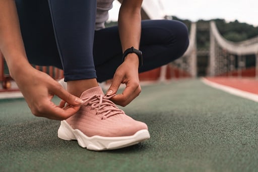 Close up of young woman getting ready for jogging outdoors while lacing her pink sneakers