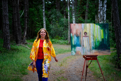 A photo of artist Ingela Johansson with her midsummer painting on an easel in the forest