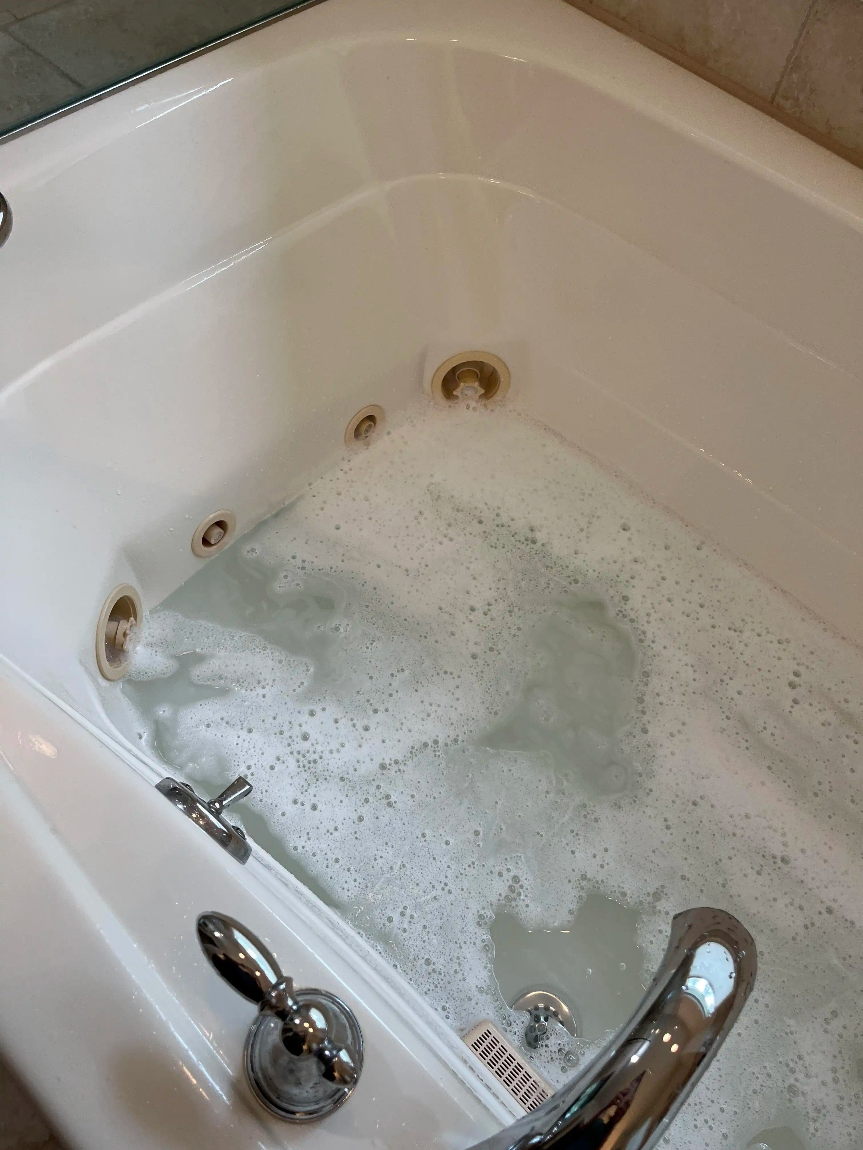 A bathtub filled with water contains numerous small black debris floating on the surface, indicating it needs cleaning. |ACE DECOR