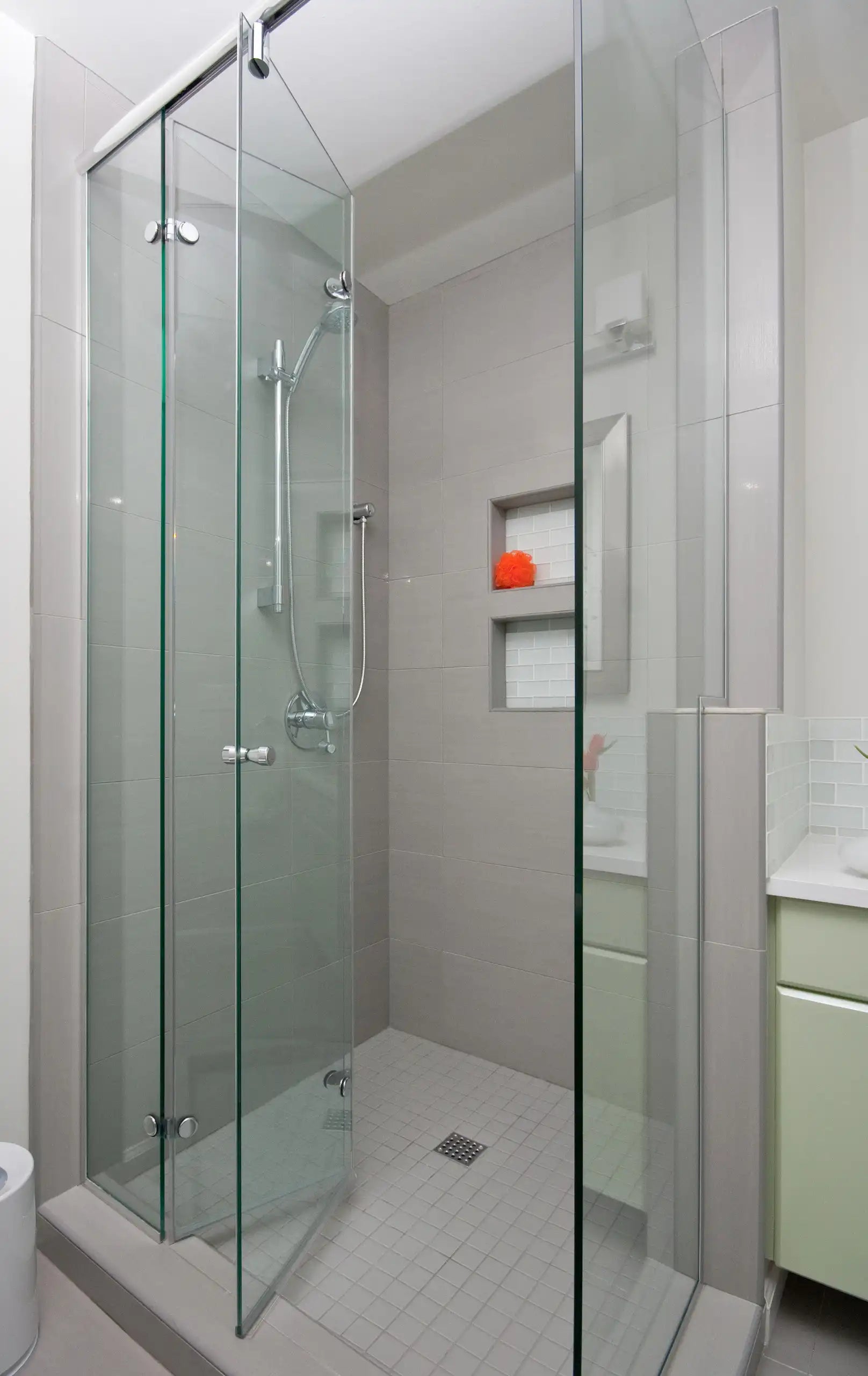 A minimalist walk-in shower featuring frameless bi-fold glass doors and built-in storage niches | ACE DECOR