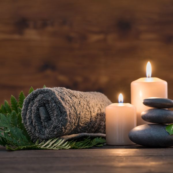 Spa setting with candles, massage stones, and a towel on a wooden surface.