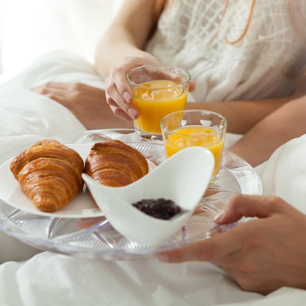 Couple enjoying a romantic breakfast in bed with fresh orange juice and croissants.