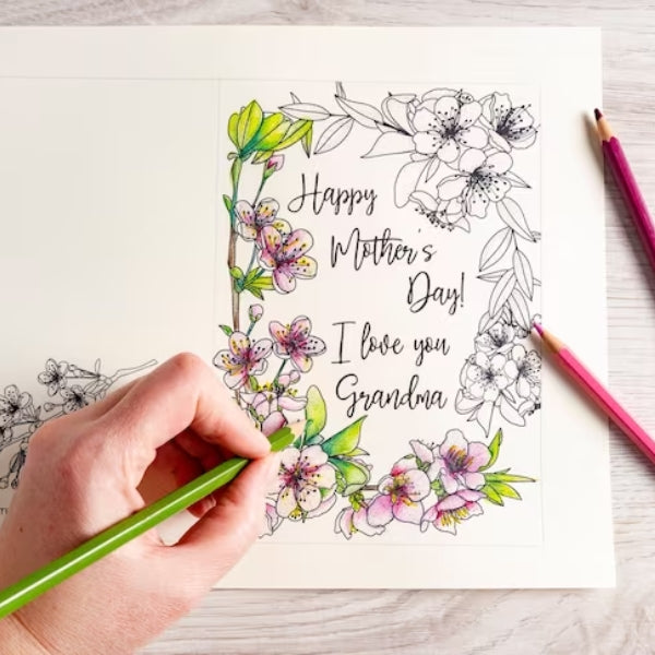 A person coloring a floral design on a mother's day card for a personalized touch