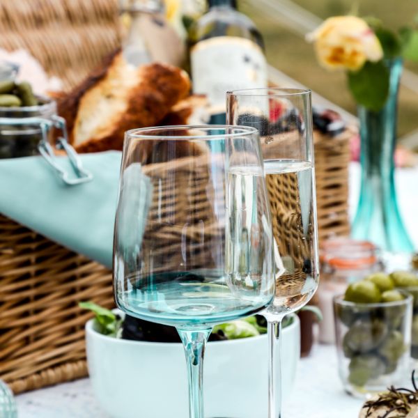 A sophisticated outdoor picnic setting featuring two glasses of sparkling wine with a background of assorted bread and olives.