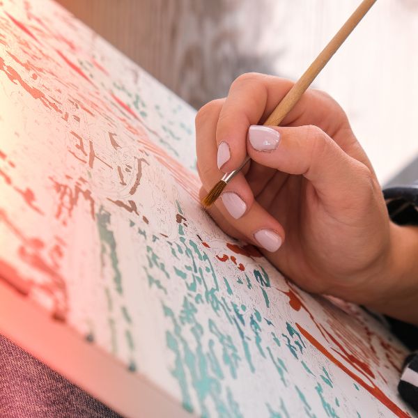 A close-up of a hand painting an abstract pattern on canvas, showing the detail and concentration involved in creating art.