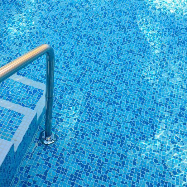 A tranquil swimming pool with clear blue water and a mosaic tile floor with a metal ladder inviting relaxation and leisure in a serene outdoor setting