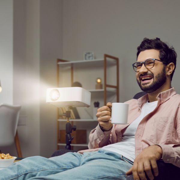 Man laughing with a coffee mug watching a movie projector at home.