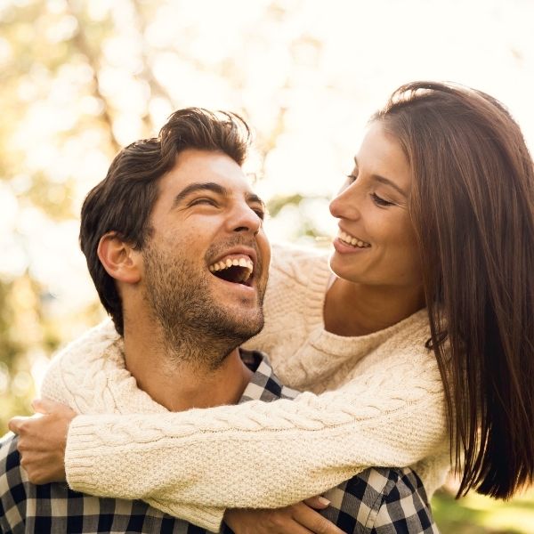 Happy couple in cozy sweaters sharing a joyful embrace outdoors.