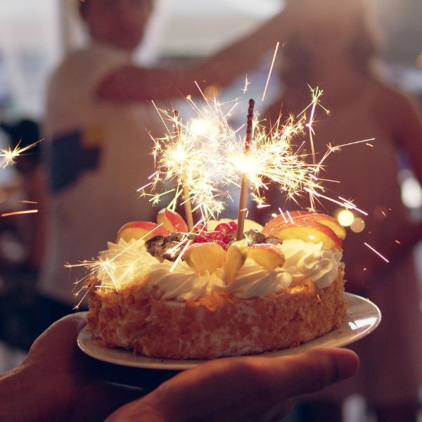 A sparkler-topped birthday cake being presented at an adult celebration to showcase birthday party ideas.