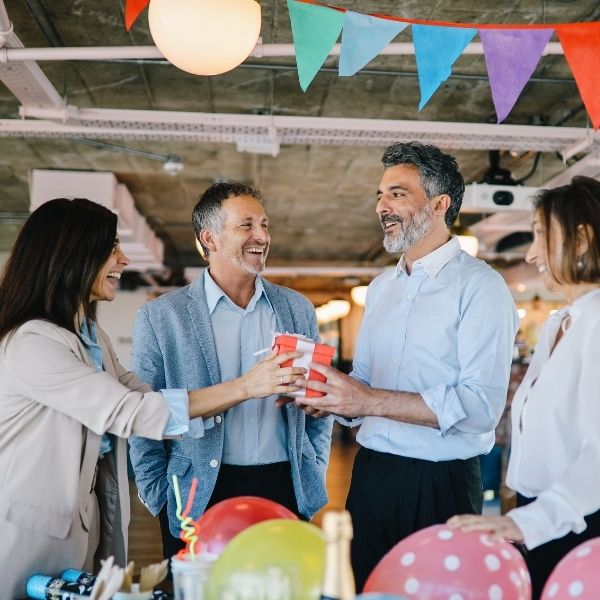 Colleagues in a festive office setting presenting a birthday gift to their boss.