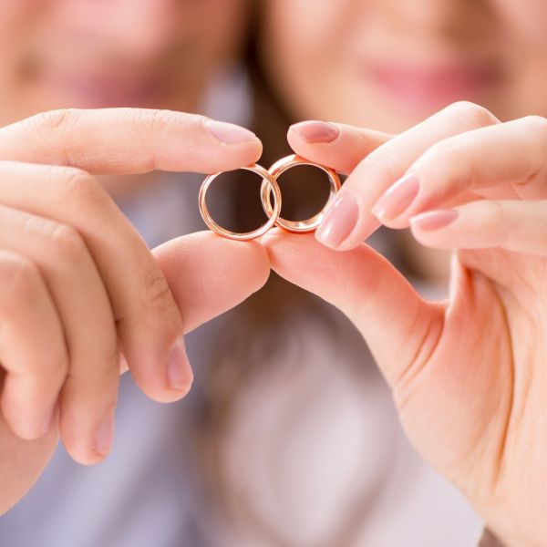 Close-up of two hands holding a pair of golden wedding rings