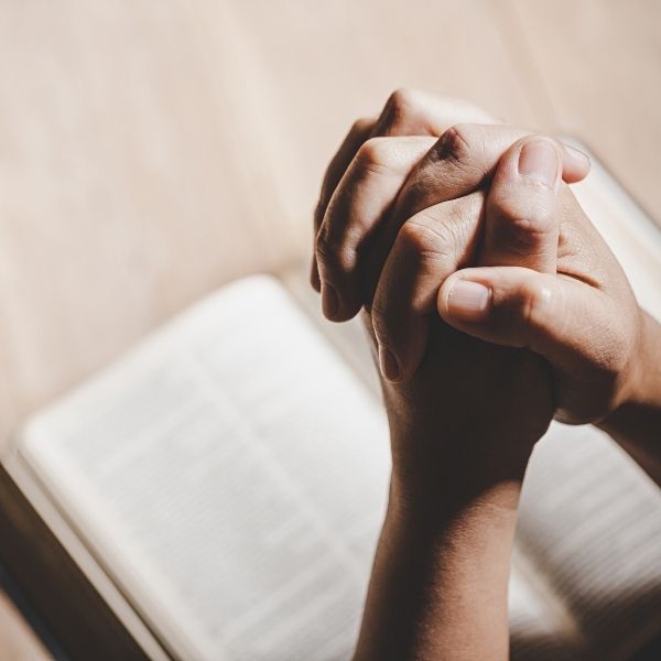 Hands held in prayer with a soft light overhead, expressing gratitude to God