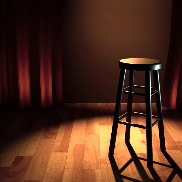 Single spotlight on an empty bar stool on stage.