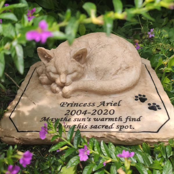 Sleeping cat memorial stone with engraved tribute, nestled in a garden setting.