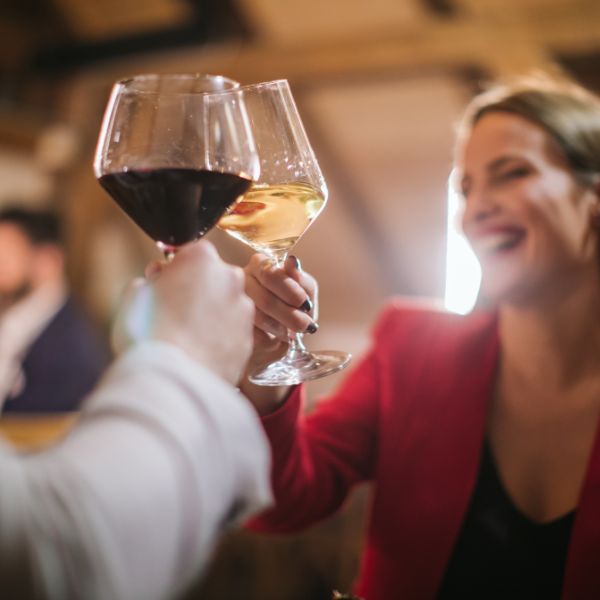 Image of a joyful woman in a red blazer toasting with a glass of white wine.