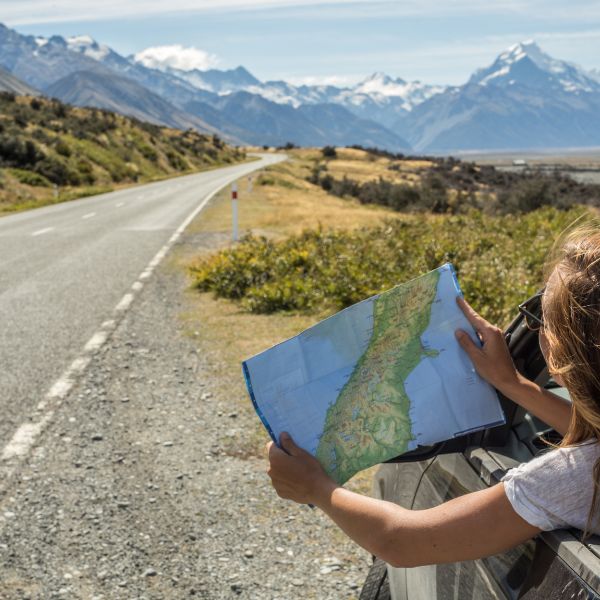 Traveler holding a map with a scenic mountain road in the background.