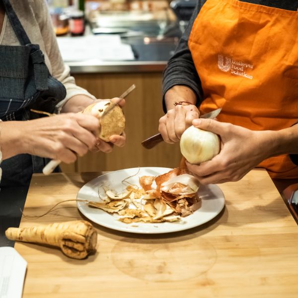 Two people peeling root vegetables over a plate, capturing the hands-on experience of cooking together in a kitchen setting.