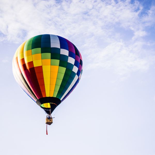 A colorful hot air balloon floats gracefully against a clear blue sky dotted with wispy clouds