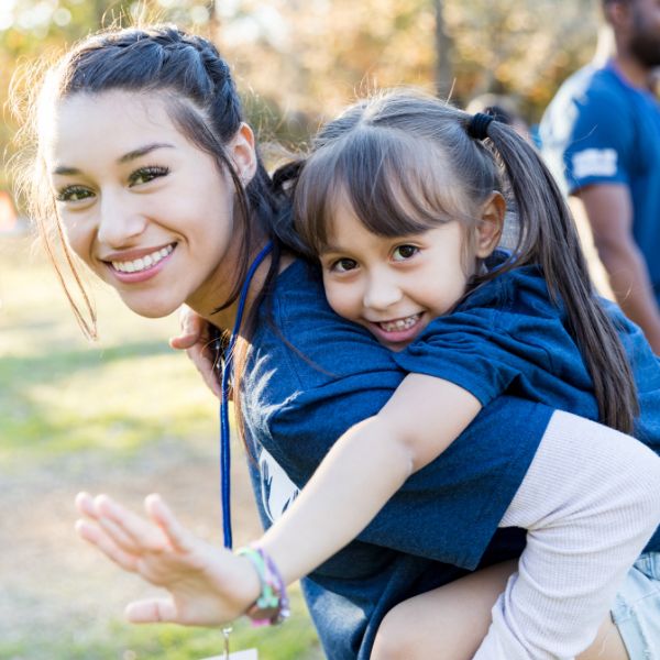 Happy volunteer carrying a child on her back at a community event.