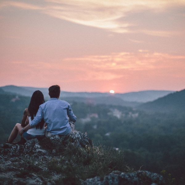 An intimate moment captured at dusk with a couple sitting on a rocky outcrop overlooking a tranquil valley.