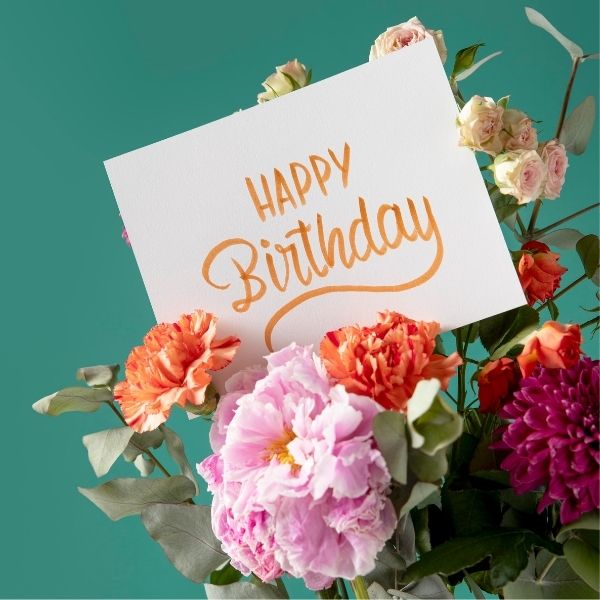 A 'Happy Birthday' card surrounded by a beautiful arrangement of colorful flowers.