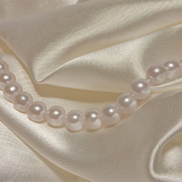A strand of pearls on silk fabric, symbolizing the traditional gifts for a 12th anniversary.