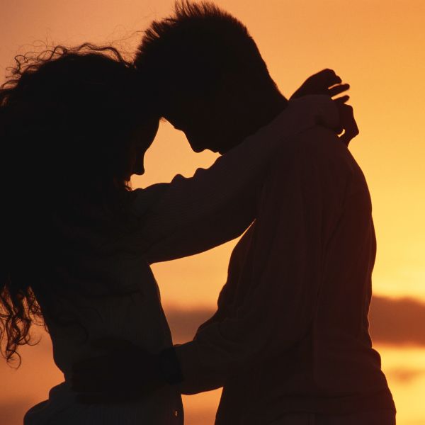 Silhouette of couple embracing on a beach at dusk.