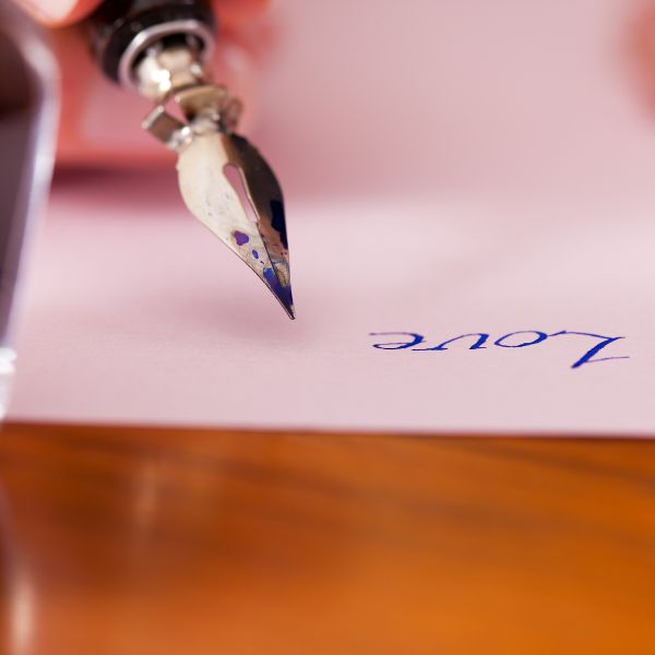 A classic fountain pen writing the word "Love" on a pink paper, emphasizing the elegance of handwritten communication.