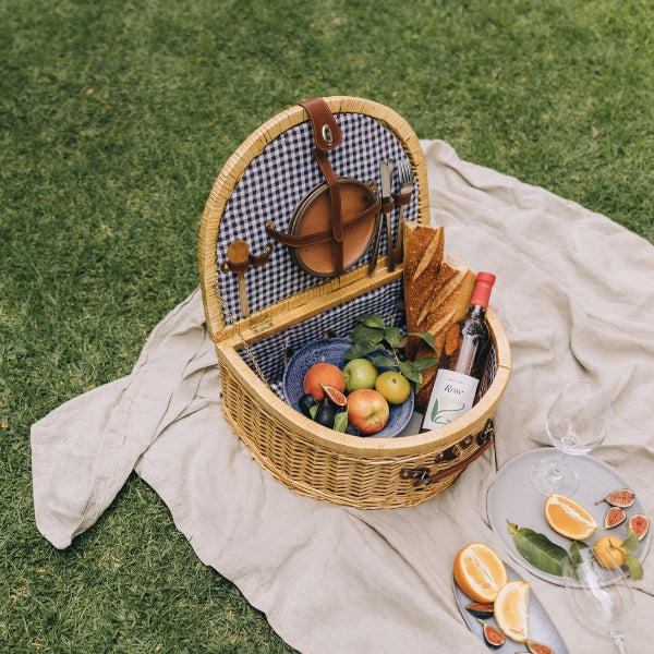 A picnic basket and blanket in a lush park setting, perfect for outdoor dining.