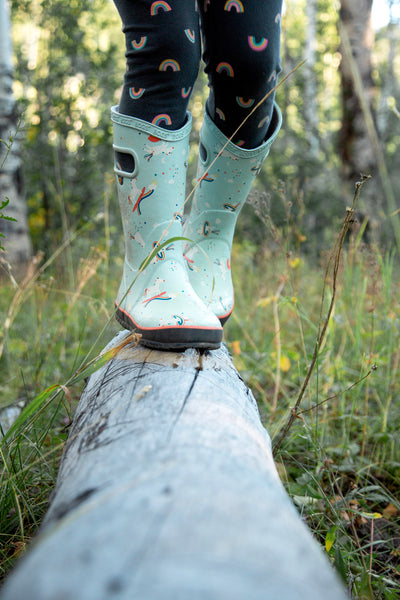 child's feet balancing on log in rainboots