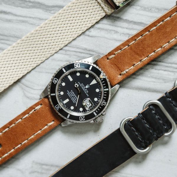 perlon watch strap and rolex submariner on a light brown leather watch strap