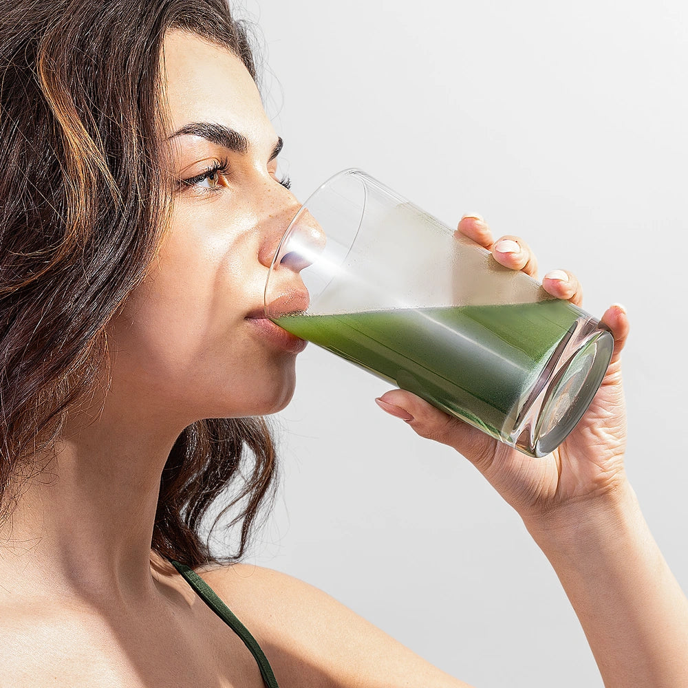 Person drinking a green smoothie from a clear glass.
