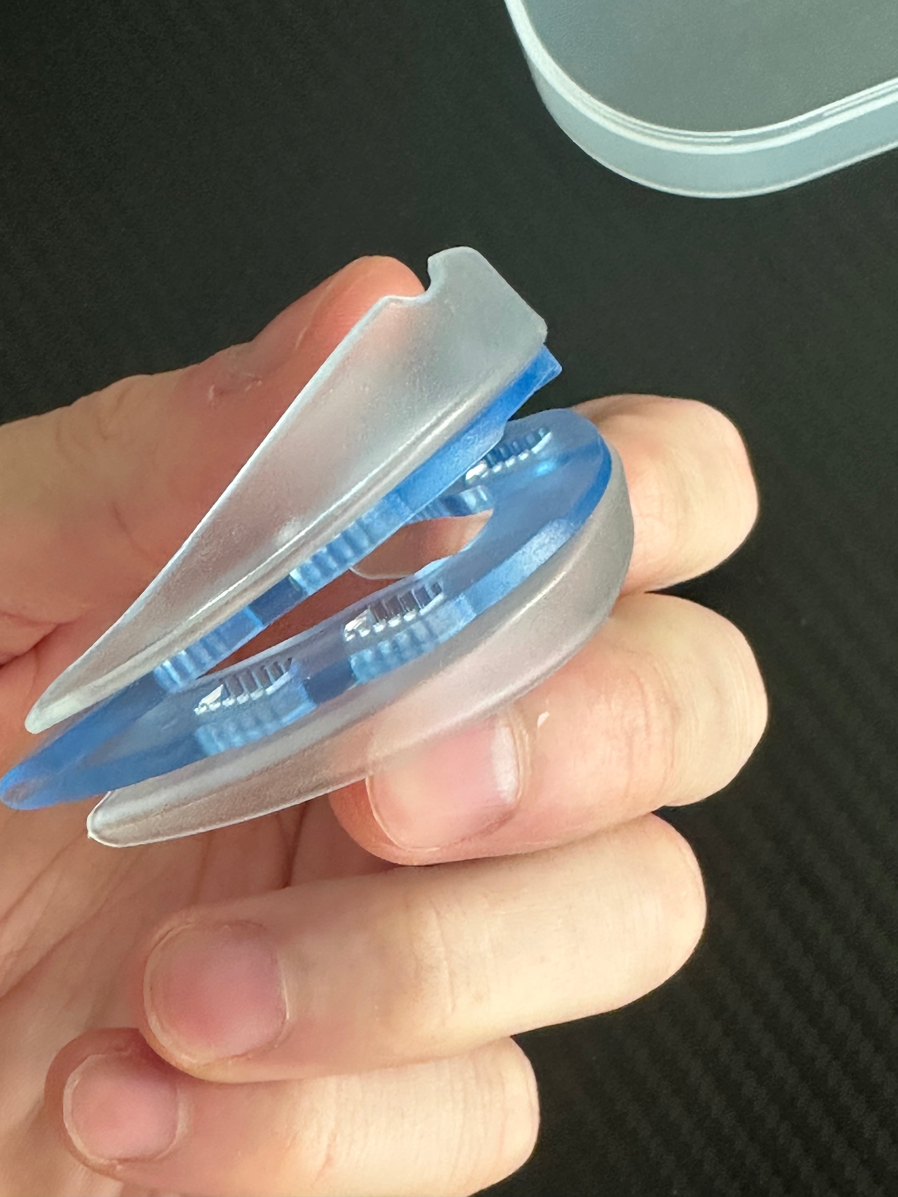 A hand holding a blue and white plastic dental device against a dark background.