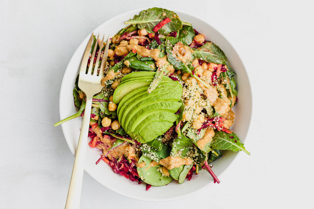 salad in white bowl from overhead with avocado, beets, carrots, chickpeas, and almond butter dressing 