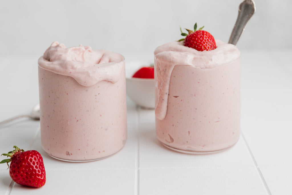 pink soft serve nice cream in two glasses with spoons and strawberry on top, on white tile surface 