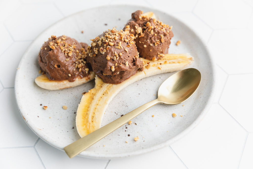 three scoops of chocolate nice cream on top of a split banana with crushed hazelnuts on top