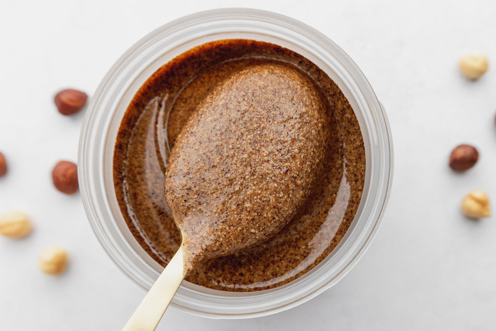 hazelnut butter in jar from overhead, with gold spoonful of nut butter being scooped out of the jar