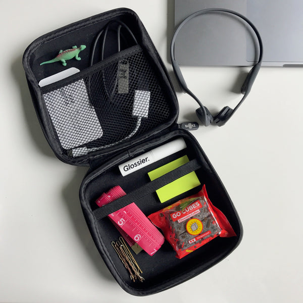 AfterShokz storage case including a headphone charger, business cards, an Apple USB adapter, lip chap, measuring tape, toy dinosaur, post it notes, bobby pins and caffeine gummies