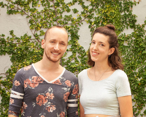 Nate, in a floral-print shirt, and Emily, in a crop top, stand in front of a vine-covered wall and smile at the camera.
