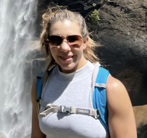 Person wearing sunglasses and hiking gear near a waterfall.