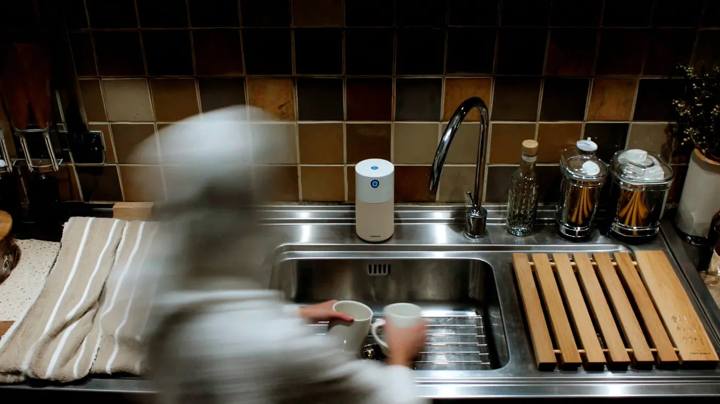 A person in a British home quickly washing a single mug in the kitchen sink, demonstrating the two-minute tidy rule.