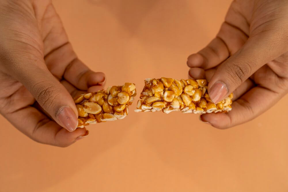 Hands holding a broken peanut bar against an orange background.