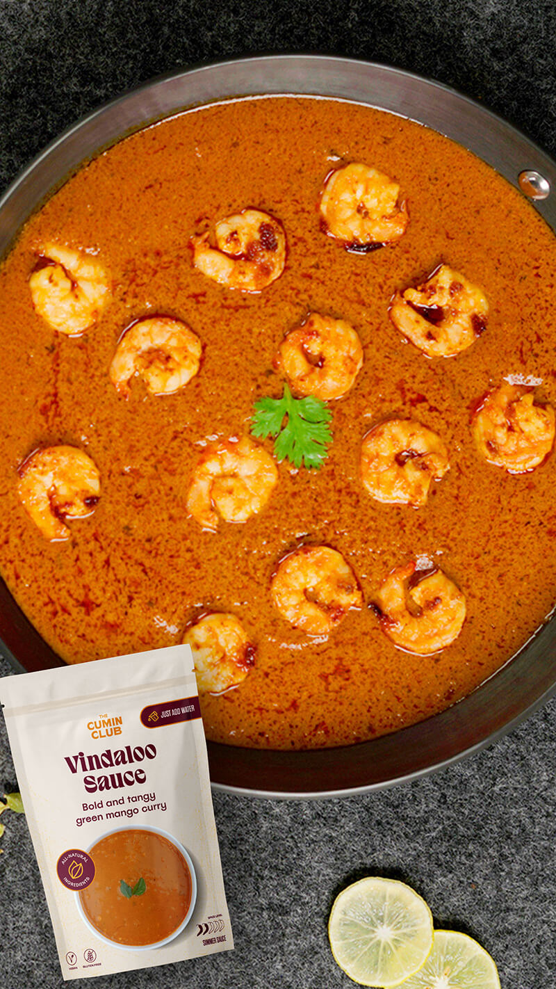 A dish of prawn curry with Vindaloo sauce and lemon slices on the side.