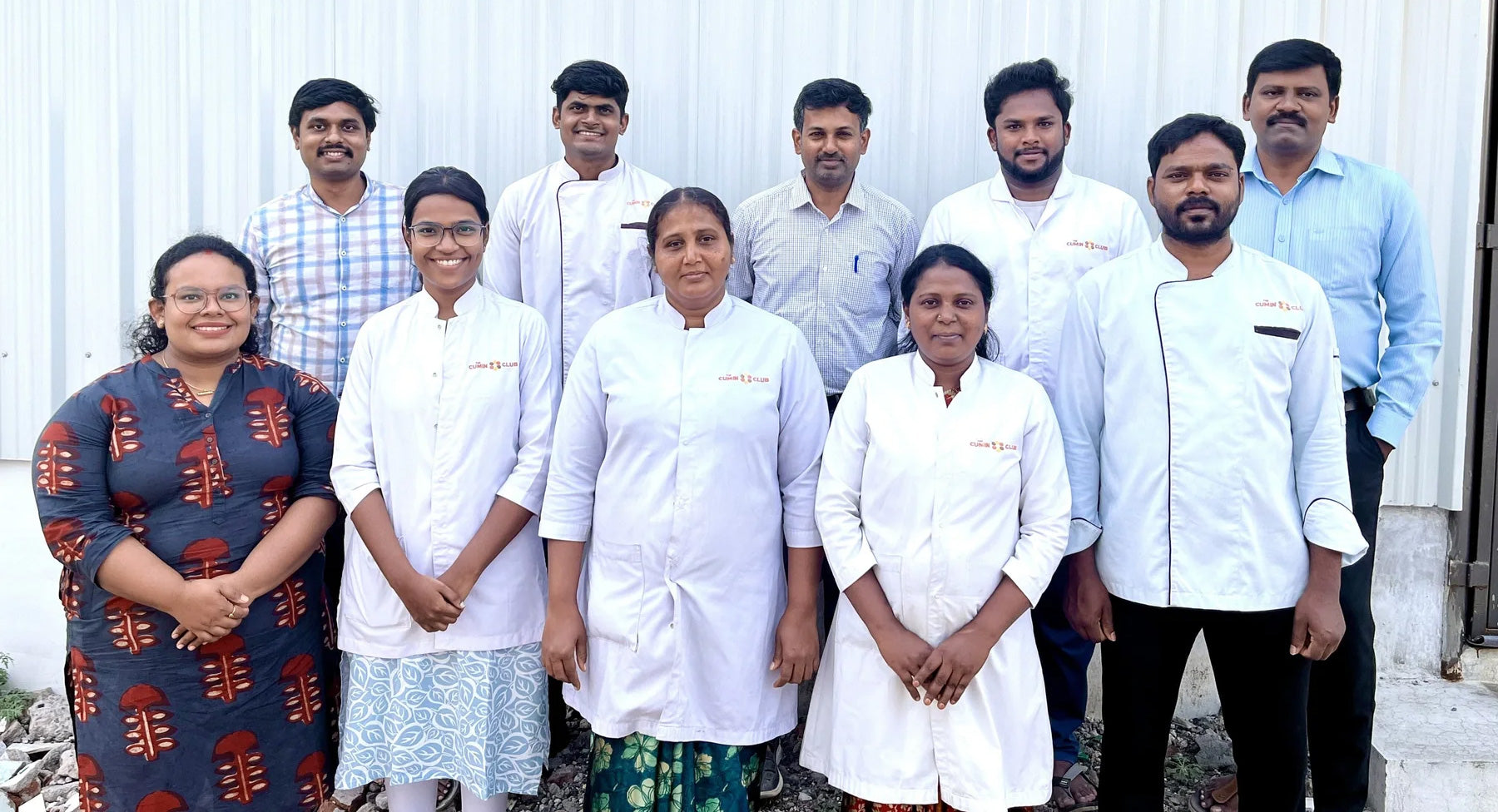 A group of ten people, some in chef uniforms, smiling outside a building.