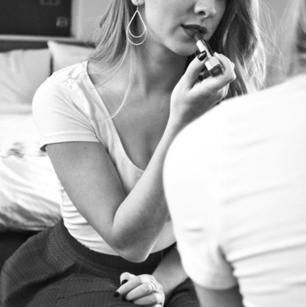 woman applying lipstick wearing handmade earrings
