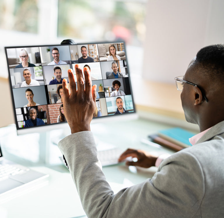 Person on video call at desk with laptop, monitor, and webcam